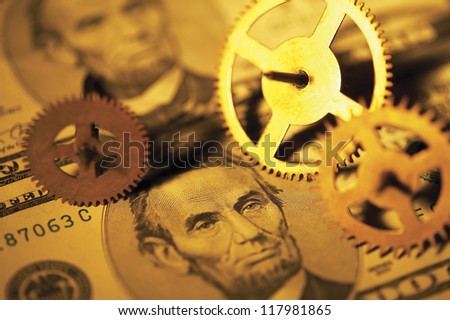 gear wheels in different sizes spread on top of american dollar bills