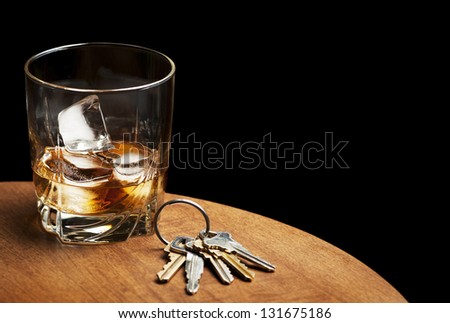 A glass of whiskey and car keys on a table with a black background.