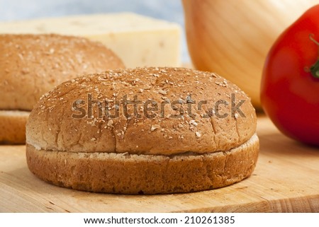 Two freshly cut hamburger buns with a tomato, an onion, and a block of cheese.