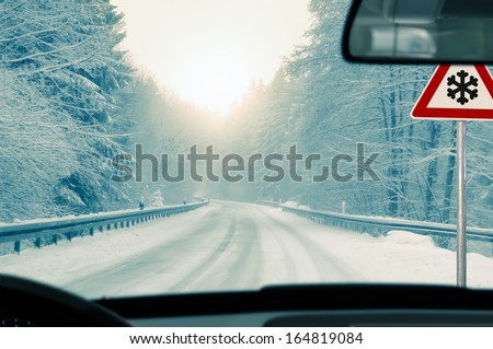 winter driving - snowy country road driving in winter - snowy country road and warning sign: risk of snow and ice