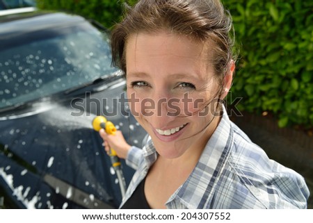 Car care - Washing a car by hand - Woman using a garden spray gun to remove the soap