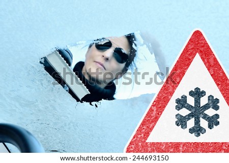 Winter Driving - Woman Scraping Ice from a Windshield - Warning Sign - The Photo has been taken from the inside of the car.