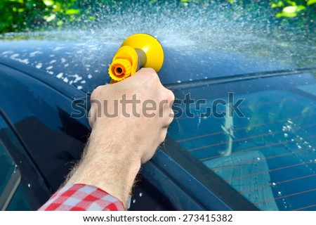Car Care - Man washing a car using a garden spray gun