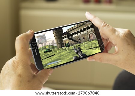 mobile gaming concept: mature woman hands with a 3d generated smartphone with game on screen