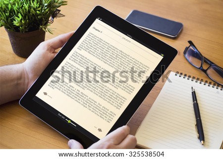hands of a man holding a book device over a wooden workspace table. All screen graphics are made up.