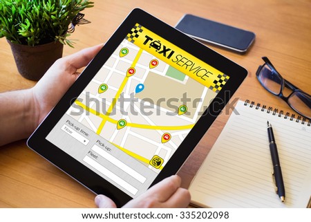 hands of a man taxi app on tablet over a wooden workspace table. All screen graphics are made up.