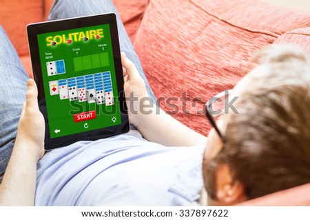 technology lifestyle concept: man on the sofa with cards game app tablet. All sreen graphics are made up