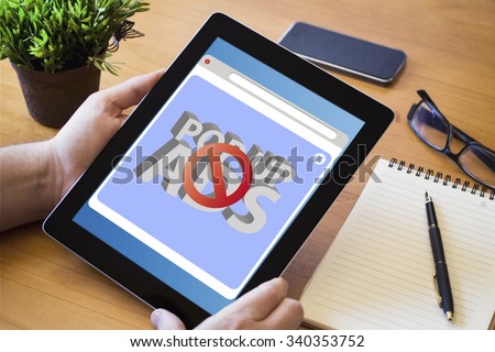 hands of a man holding a device with ads blocker on the screen over a wooden workspace table. All screen graphics are made up.