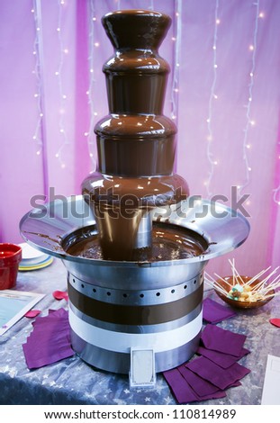 Melting chocolate drips down the different tiers of a chocolate fountain structure.