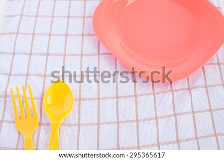 yellow fork and spoon, pink plastic plate on tablecloth background