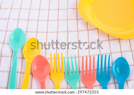colorful fork and spoon, yellow plastic plate on tablecloth background