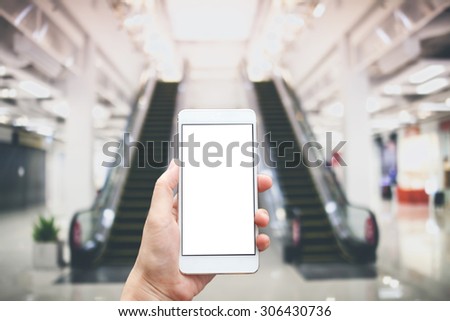 Business conceptual- Focused on left hand holding mobile on escalator at shopping mall blurred background