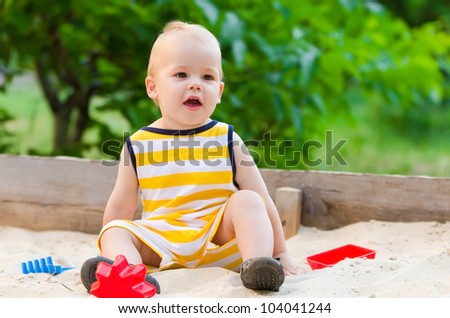 The nice smiling boy playing sand with toys