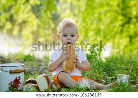 the lovely little boy sitting on a plaid and eating bread with milk