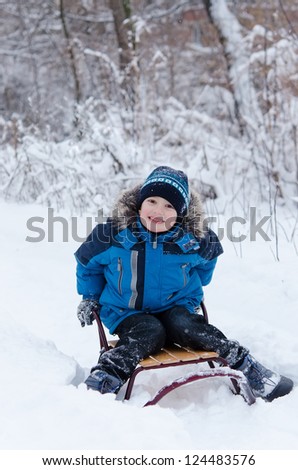 Lovely little boy having fun on sledge on winter snow day