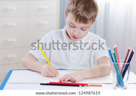 Cute boy at the table with color pencils drawing at home