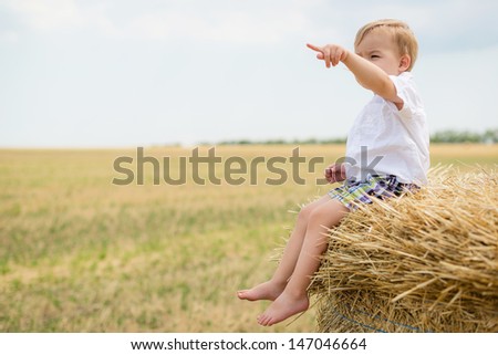 Little lovely boy on golden hay field with huge straw bale