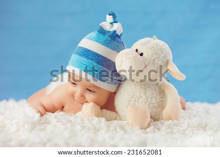 Smile baby in hat, hugging toy on a white bedspread, on a blue background
