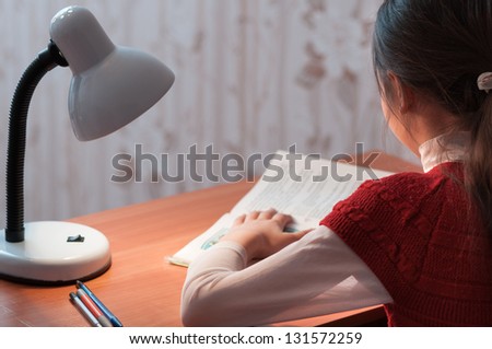 the girl at the desk reading a book by the light of the lamp