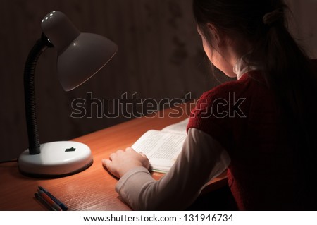 the girl at the desk reading a book by the light of the lamp