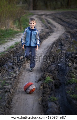 boy playing with a ball on the mud road after rain
