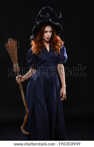 Young beautiful red-haired witch with a broom in the dark