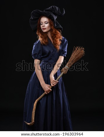Young beautiful red-haired witch with a broom in the dark