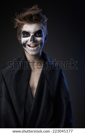 Teen with make-up of the skull in a black cloak laughs