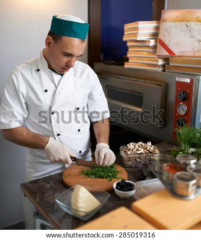 Chef in the kitchen cut parsley pizza