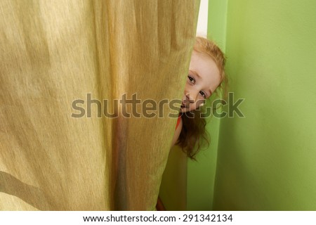 cheerful girl looks out from behind the curtains