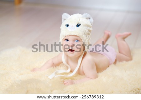 6 month blue-eyed baby in beige hat with blue eyes and ears on a beige fur on the floor