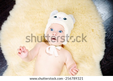6 month blue-eyed baby in beige hat with blue eyes and ears on a beige fur on the floor