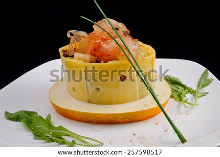 Salad in a plate of cheese and melon with ham, potatoes, cucumber, bacon, greens, watered transparent syrup and decorated with green leaves on a white plate