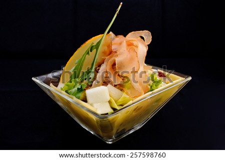 Beautiful salad with bacon, peach, cheese, potatoes, salad, green, clear sauce, served in a glass salad bowl on a black background