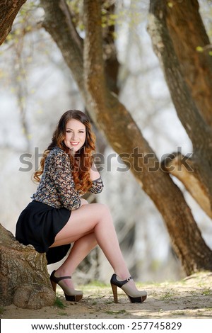 Beautiful young girl with orange hair on nature near a tree in a short skirt