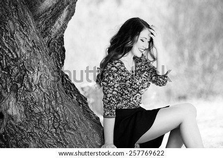 Beautiful young girl with long hair on nature near a tree in a short skirt, black and white