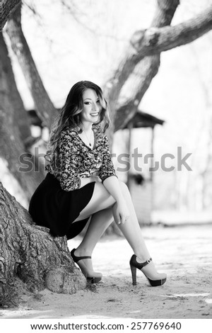 Beautiful young girl with long hair on nature near a tree in a short skirt, black and white