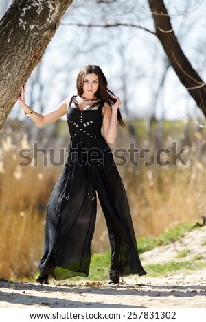 Beautiful girl in a black suit with long brown hair, shapely long legs and large breasts posing in nature. Brunette in a black suit in the nature. Blue-eyed brunette in black with big breasts.