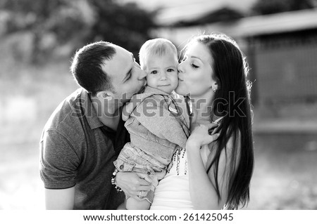 Happy family, mother and father kissing son, 1 year old, black and white, happy, love. Against the background of trees in a city park.