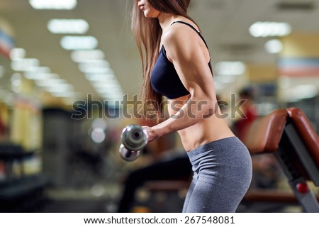 Brutal athletic woman pumping up muscles with barbell. Attractive fitness woman, trained female body. Brunette sexy fitness girl in black and gray sport wear with perfect body in the gym.