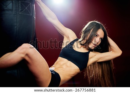 Sporty sexy girl with great abdominal muscles in a black sportswear near the punching bag on a red wall. Fitness girl posing in a boxing gym. Brunette in the gym.