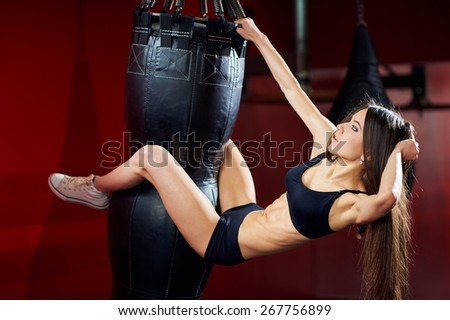 Sporty sexy girl with great abdominal muscles in a black sportswear near the punching bag on a red wall. Fitness girl posing in a boxing gym. Brunette in the gym.