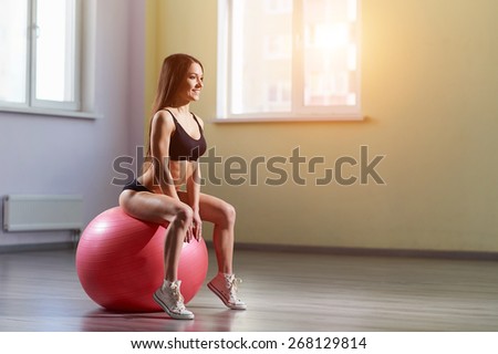 Fitness woman in gym resting on pilates ball. Young woman doing exercise on fitness ball. Young girl on the pink fitness ball in gym. Girl with fitness ball. Beautiful girl doing exercises with ball.