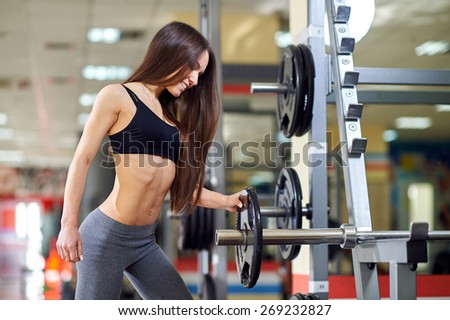 Athletic girl doing exercises with barbell in gym. Attractive fitness woman, trained female body. Brunette sexy fitness girl in black and gray sport wear with perfect body in the gym.
