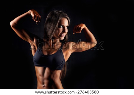 Sporty sexy girl with great abdominal muscles in black sportswear. Tanned young sexy athletic girl. A great sport female body. The girl athlete demonstrates chiseled biceps. Miss fitness bikini