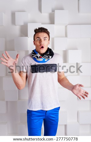 cool stylish trendy sports emotional guy with styled hair in white t-shirt, scarf around his neck and blue pants, white sneakers posing in Studio on white background squares with a shocked expression