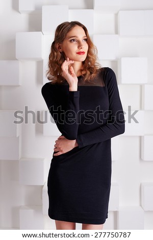 stylish fashionable girl with wavy hair and red lipstick, red shoes in a short black dress stands on a background of white squares in the Studio