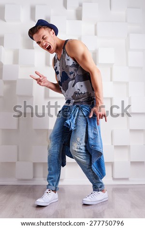 cool stylish trendy sports guy in the hat  in jeans Boyfriends in multi-colored t-shirt and tied at the waist denim jacket in white sneakers in Studio on white background squares dancing to rock music