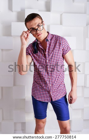 stylish trendy athletic guy in tight blue shorts and a plaid shirt with bow tie in points in the multi-colored loafers with the white squares in the Studio