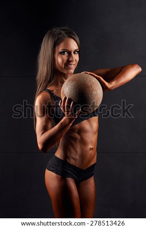 Sports sexy girl with nice abs and toned elastic buttocks in black sportswear. Tanned young sports girl holding a metal ball . The sport of female body. The girl athlete, muscular body. Miss bikini